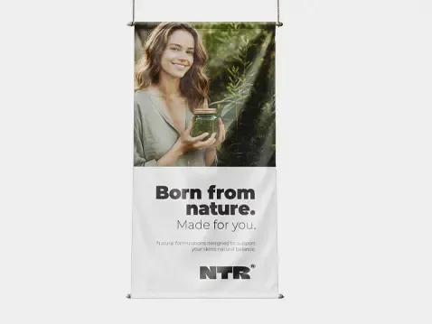 Baner tekstylny z hasłem Born from nature. Made for you. oraz zdjęciem uśmiechniętej kobiety trzymającej słoik z naturalnym produktem