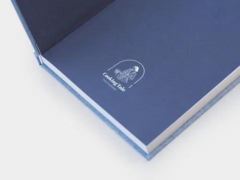 Zbliżenie na wewnętrzną stronę twardej oprawy notesu książkowego A5 z nadrukowanym logo na granatowej wyklejce.