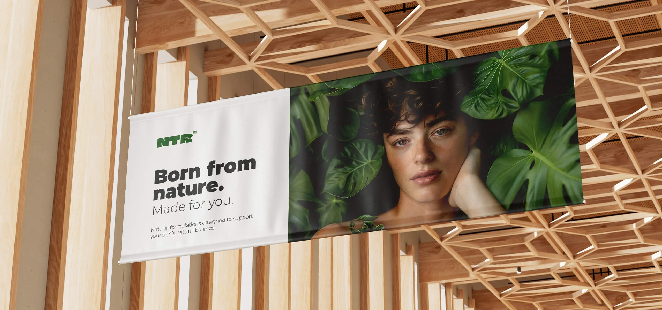 Matowy baner tekstylny z hasłem Born from nature. Made for you. oraz portretem modela wśród zielonych liści